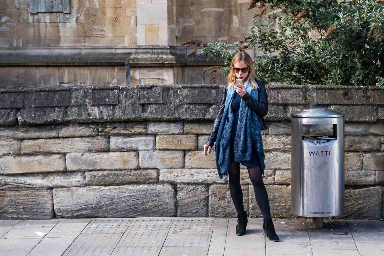 Bir kadın sokakta telefon elinde ve sigara içiyor. Mesajlarını okuyor